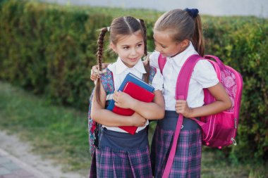 Okul terasında kitapla ayakta duran iki gülümseyen okul çocuğunun portresi