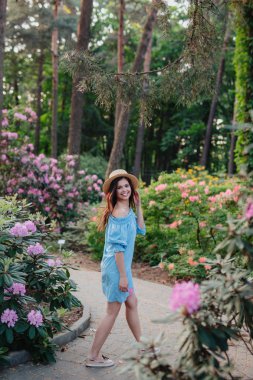 Pembe çiçekler yanında duran mavi vintage elbise ve hasır şapka güzel kız.