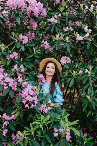 Retrato de una joven hermosa mujer en sombrero de paja posando entre árboles florecientes — Foto de Stock