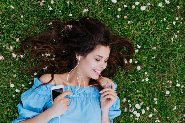 Όμορφη γυναίκα ακούγοντας μουσική με ακουστικά και κείτεται σε έναν κήπο με λουλούδια — Φωτογραφία Αρχείου