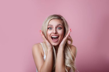 Sürpriz güzel kadın pembe stüdyo arka plan üzerinde elle yanakları tutar