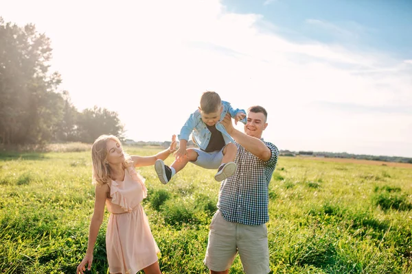 Madre y padre balanceándose hijo en soleado día de verano — Foto de Stock