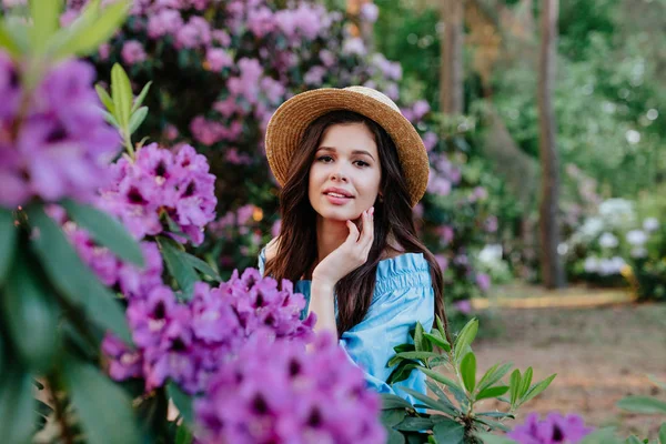 Beautiful girl in blue vintage dress and straw hat standing near pink flowers. — Stock Photo, Image