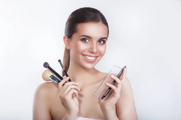 Close-up de belo jovem modelo feminino sorridente com escovas cosméticas e sombra de olhos no fundo branco . — Fotografia de Stock