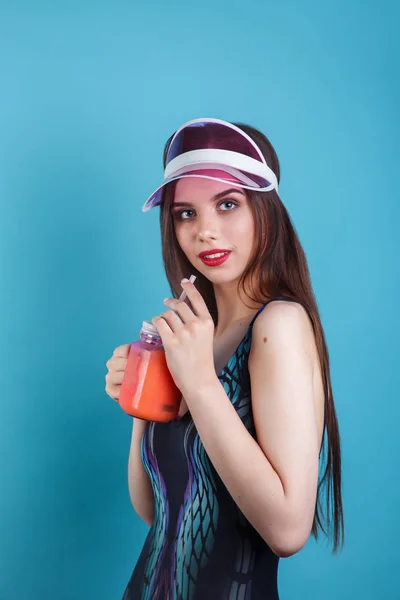 青い背景に新鮮な夏の飲み物のガラスを保持水着とプラスチックバイザーでセクシーな女性 — ストック写真