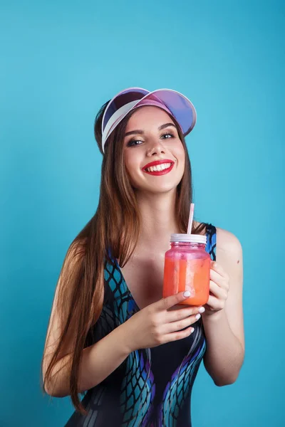 Femme sexy en maillot de bain et visière en plastique tenant verre de boisson fraîche d'été sur fond bleu — Photo