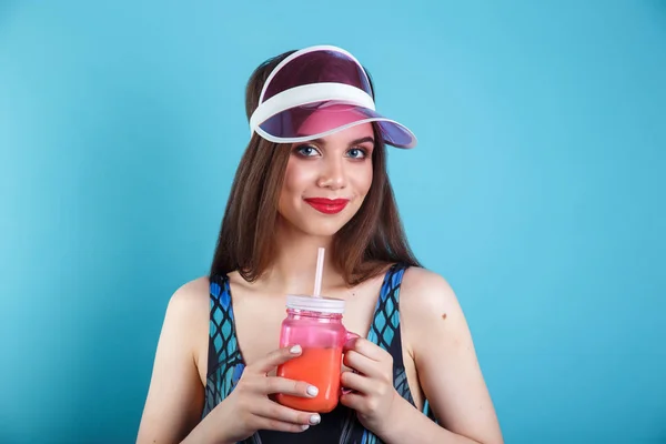Sexy žena v plavkách a plastovém štítu držící sklenici čerstvého letního nápoje na modrém pozadí — Stock fotografie