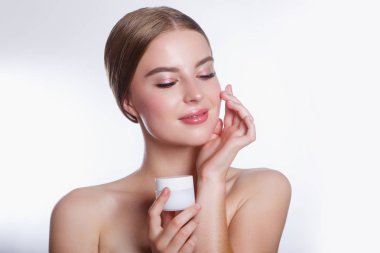Yüzünde nemlendirici krem uygulayarak güzel bir kadın. Kız elinde krem tutuyor. Spa ve yüz bakımı