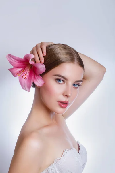 Mujer hermosa joven con flor de lirio rosa sobre fondo gris. Concepto de cuidado de la piel — Foto de Stock