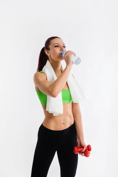 beautiful strong happy cheerful young sports woman posing indoors drinking water with towel on neck.