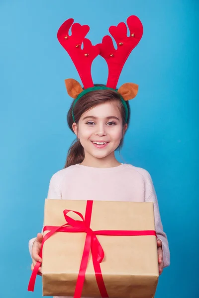 Улыбающийся смешной ребенок с оленьими рогами, держащий в руках рождественский подарок. Концепция Рождества . — стоковое фото