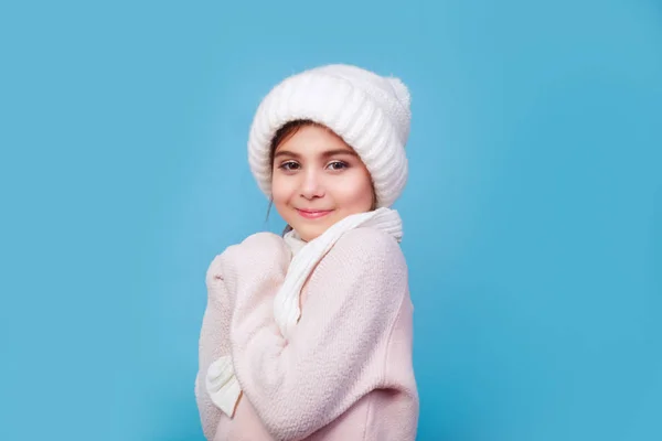 Retrato de invierno de una linda niña sonriente con sombrero blanco de punto, bufanda y suéter sobre fondo azul . — Foto de Stock