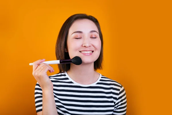 Cabelo curto mulher asiática aplicando escova de pó cosmético no fundo amarelo — Fotografia de Stock