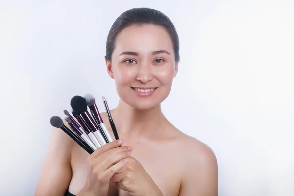 Belle fille asiatique avec ensemble de cosmétiques. Femme witn maquillage naturel souriant et tenant collection de brosses à poudre — Photo