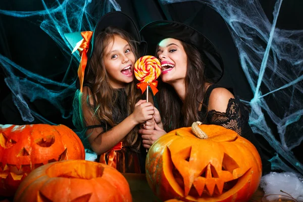 Mutter und Tochter in Hexenkostümen feiern Halloween mit Halloween-Bonbons und Süßigkeiten über Spinnennetz — Stockfoto