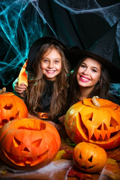 Close-up mooie blanke moeder en haar dochter in heks kostuums vieren Halloween poseren met gebogen pompoenen — Stockfoto
