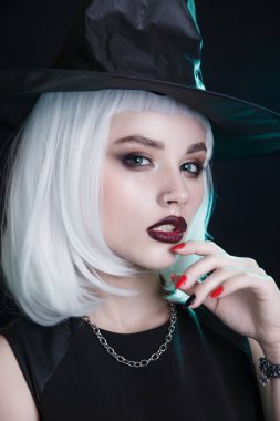 Cadılar Bayramı 'nda siyah dudaklı ve beyaz saçlı seksi cadı siyah stüdyo arkaplanındaki kameraya bakıyor.