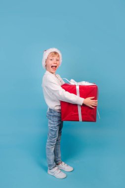 Noel Baba kırmızı şapkalı komik çocuk mavi arka planda elinde Noel hediyesi tutuyor. Noel konsepti.
