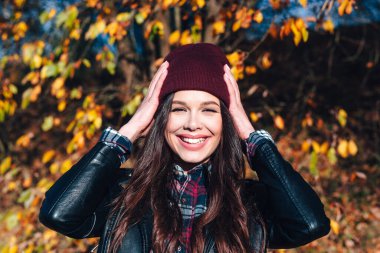 Sonbahar parkında şapkalı ve ekose gömlekli mutlu genç bir kadın.