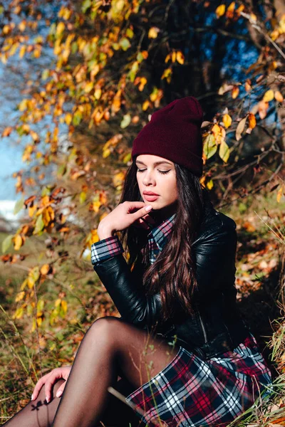 Pretty young happy woman in stylish clothes sitting in autumn park — Stock Photo, Image