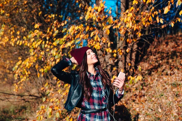 Young woman in plaid shirt listening to the music in autumn park — Stock Photo, Image