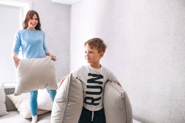 Oğlu ve annesi güneşli bir sabahta evde yastık kavgası yapıyor.