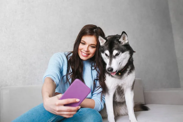 Glad ung kvinna tar en selfie med husky hund hemma — Stockfoto