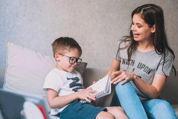 A kisfiú házi feladatot csinál otthon, iskolai könyvekkel és laptoppal, az anyja segítségével.. — Stock Fotó