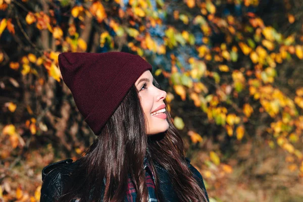 Happy young woman in a hat and a plaid shirt in autumn park looking away — Stock Photo, Image