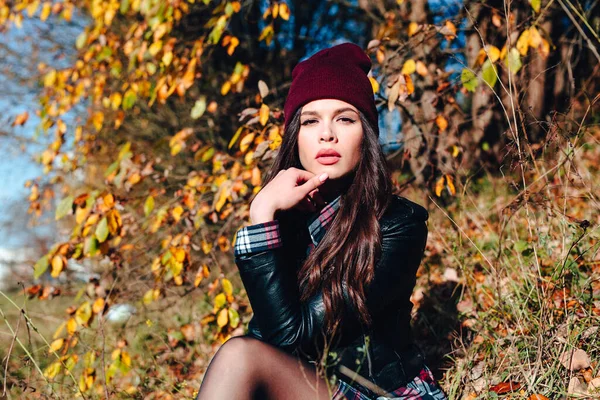 Pretty young happy woman in stylish clothes sitting in autumn park — Stock Photo, Image