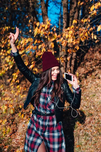Hermosa chica escuchando música en el teléfono inteligente y bailando en el parque de otoño — Foto de Stock