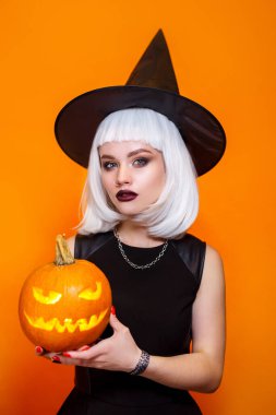 Turuncu arka planda oyulmuş balkabağı olan seksi cadılar bayramı cadısı. Mutlu Cadılar Bayramı