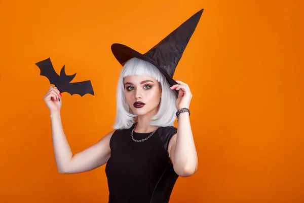 Young woman in hat and dress as a witch on orange background — Stock Photo, Image