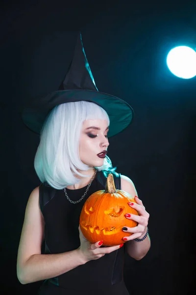 Sexy jeune femme en chapeau de sorcières et costume tenant citrouille sur fond noir — Photo