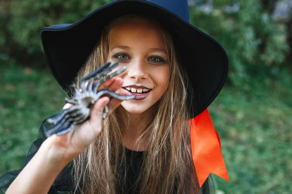 Menina em traje de bruxa se divertindo com aranha ao ar livre — Fotografia de Stock
