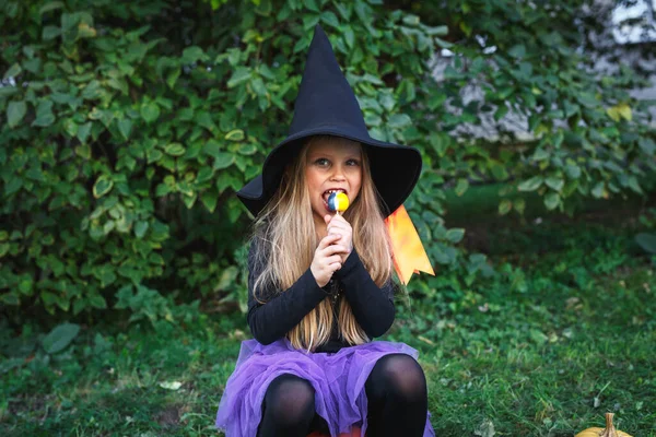 Chica divertida en traje de bruja comiendo dulces de Halloween al aire libre — Foto de Stock