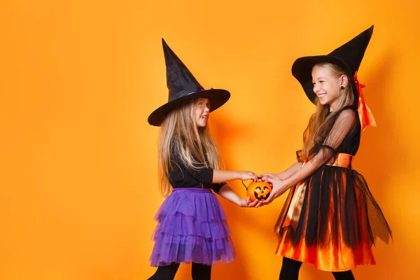 Glückliche Kindermädchen in Hexenkostümen auf orangefarbenem Hintergrund — Stockfoto