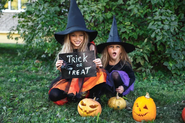 Twee kleine meisjes in heksenkostuums die plezier hebben op Halloween buiten. Snoep of je leven — Stockfoto