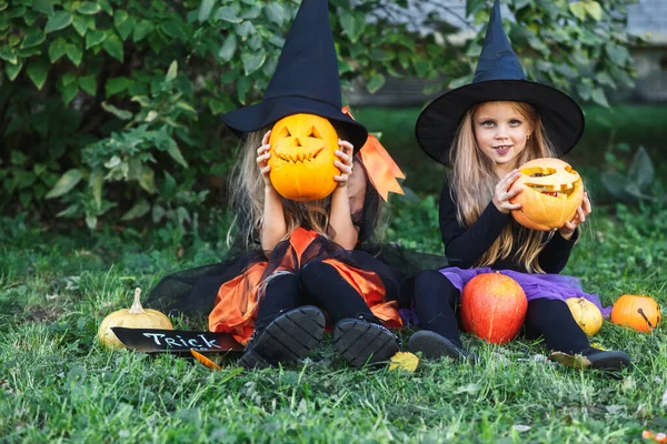 Feliz Halloween. Dos niños divertidos en trajes de bruja y con calabazas sentadas al aire libre — Foto de Stock