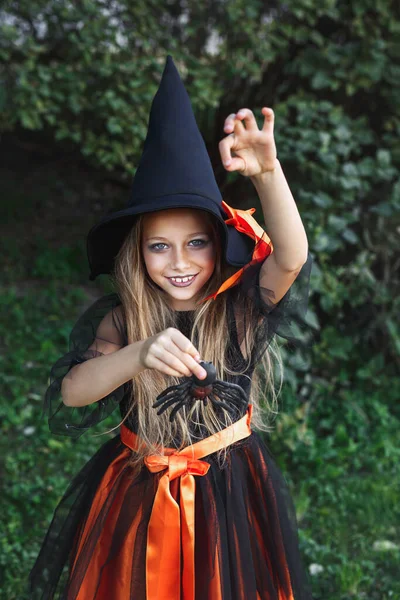 Niña en traje de bruja divirtiéndose con araña al aire libre — Foto de Stock