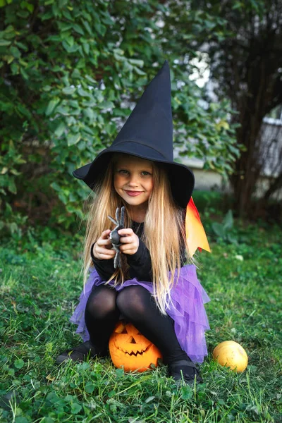 Cadılar Bayramı için cadılar bayramı kostümlü komik kız dışarıda balkabağı Jack 'in üzerinde oturuyor. — Stok fotoğraf