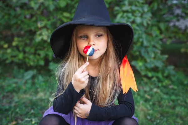 Забавная девочка в костюме ведьмы ест конфеты на открытом воздухе на Хэллоуин — стоковое фото