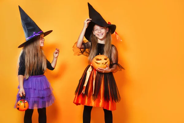 Két kislány halloween jelmezek szórakozás narancssárga stúdió háttér — Stock Fotó