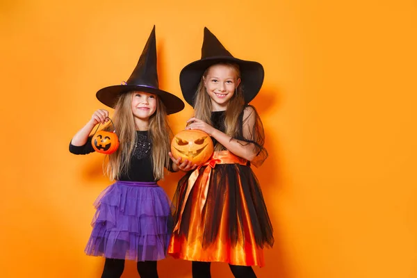 Cadılar Bayramı kostümlü iki küçük kız turuncu stüdyoda eğleniyor. — Stok fotoğraf