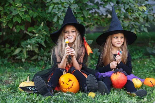 Twee grappige meisjes in heksenkostuums die Halloween snoep eten. — Stockfoto