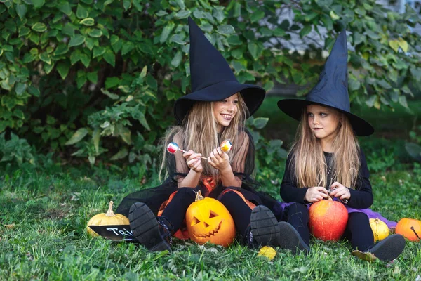 Due sorelline divertenti in costume da strega che mangiano caramelle di Halloween — Foto Stock