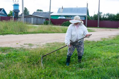 Bir kadın bulutlu bir yaz gününde tırpanla taze yeşil çimen biçiyor..