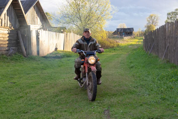 A man rides a motorcycle on a village road.