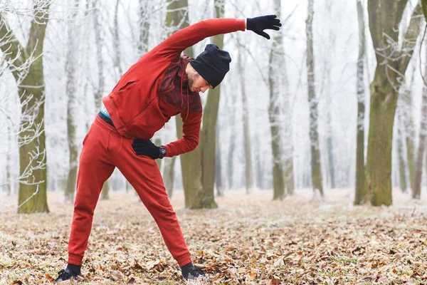 Young male jogger stretching arms muscles and warming up before running outdoors in winter.