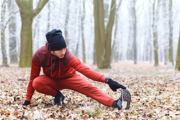 Young male jogger warming up before running outdoors in winter